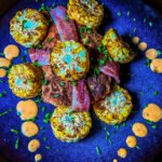 chicken breast wrapped in bacon with corn on the cob pieces and sauce on a place.