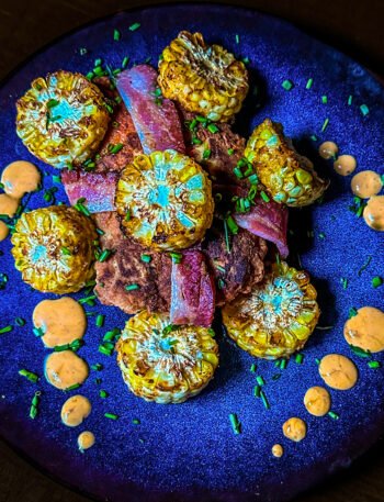 chicken breast wrapped in bacon with corn on the cob pieces and sauce on a place.