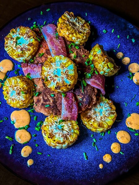 chicken breast wrapped in bacon with corn on the cob pieces and sauce on a place.