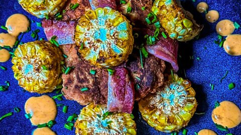 chicken breast wrapped in bacon with corn on the cob pieces and sauce on a place.