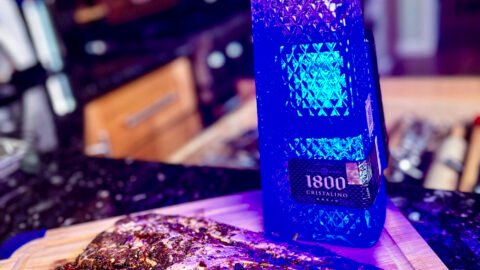 iberico pork on a wooden cutting board next to a bottle of blue illuminated tequila.
