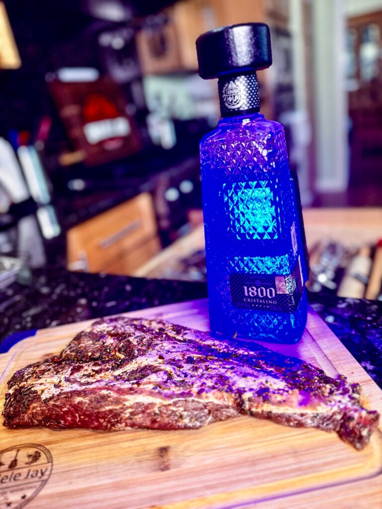 iberico pork on a wooden cutting board next to a bottle of blue illuminated tequila.
